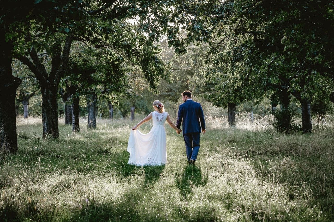 A newly-married couple elegantly walk away from their wedding and stroll through a springtime meadow