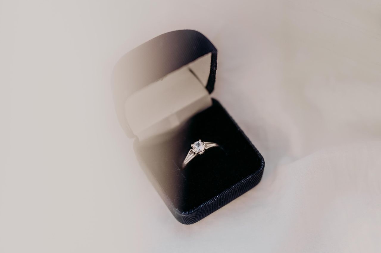 A detail shot of a vintage-inspired solitaire ring in a black ring box on white fabric