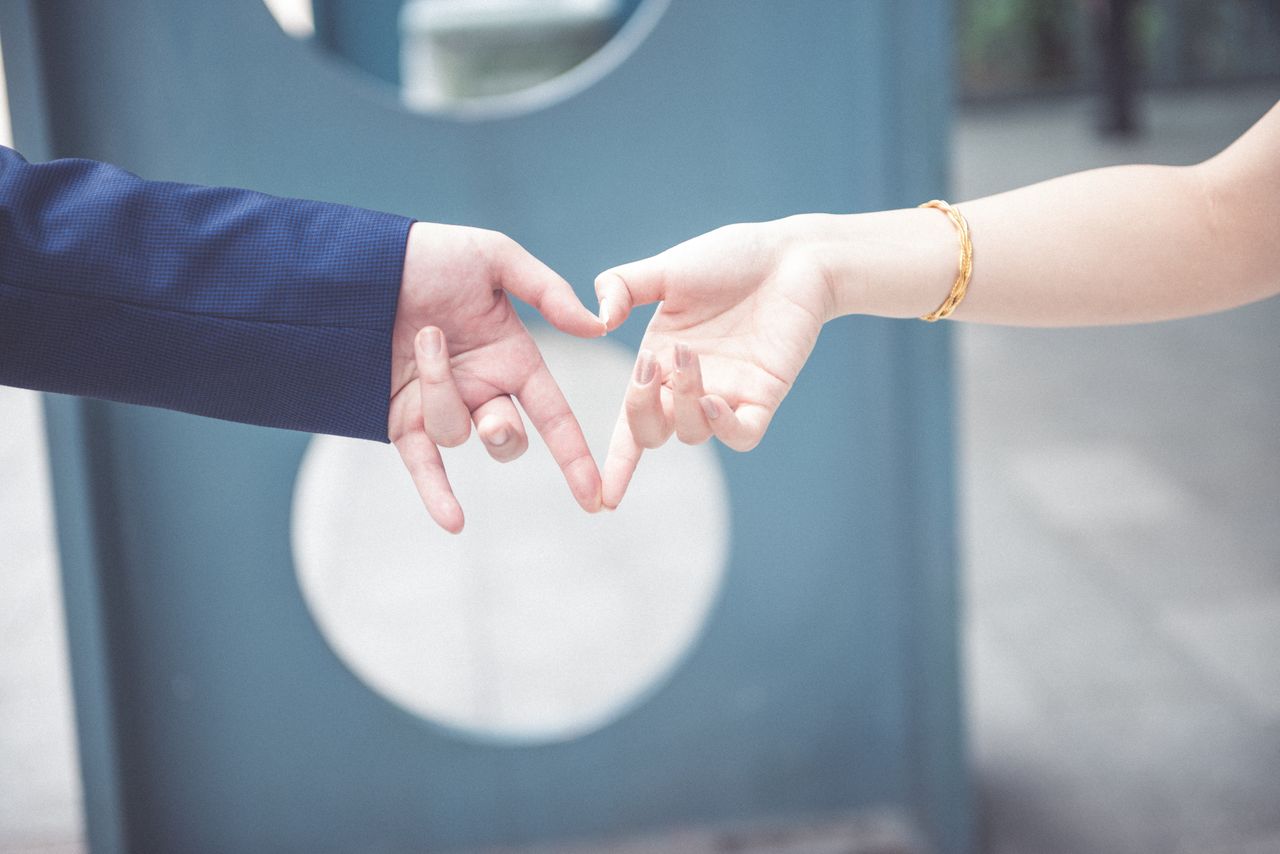 Two people join their hands together to form a heart. One is wearing a gold bangle that can hold an engravement on the inside