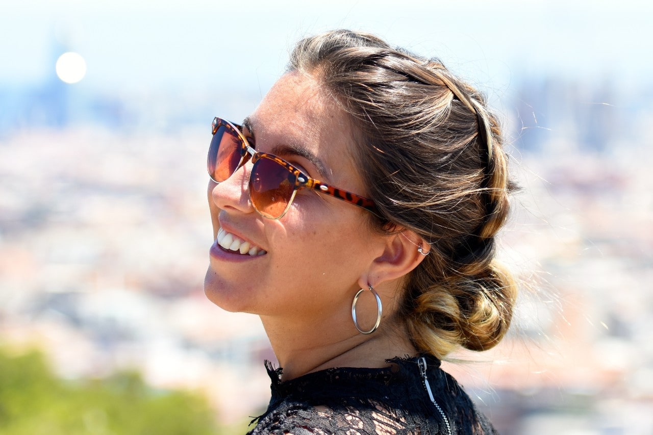A woman outside with sunglasses and hair in a bun wearing hoop earrings and a hoop through her cartridge as well