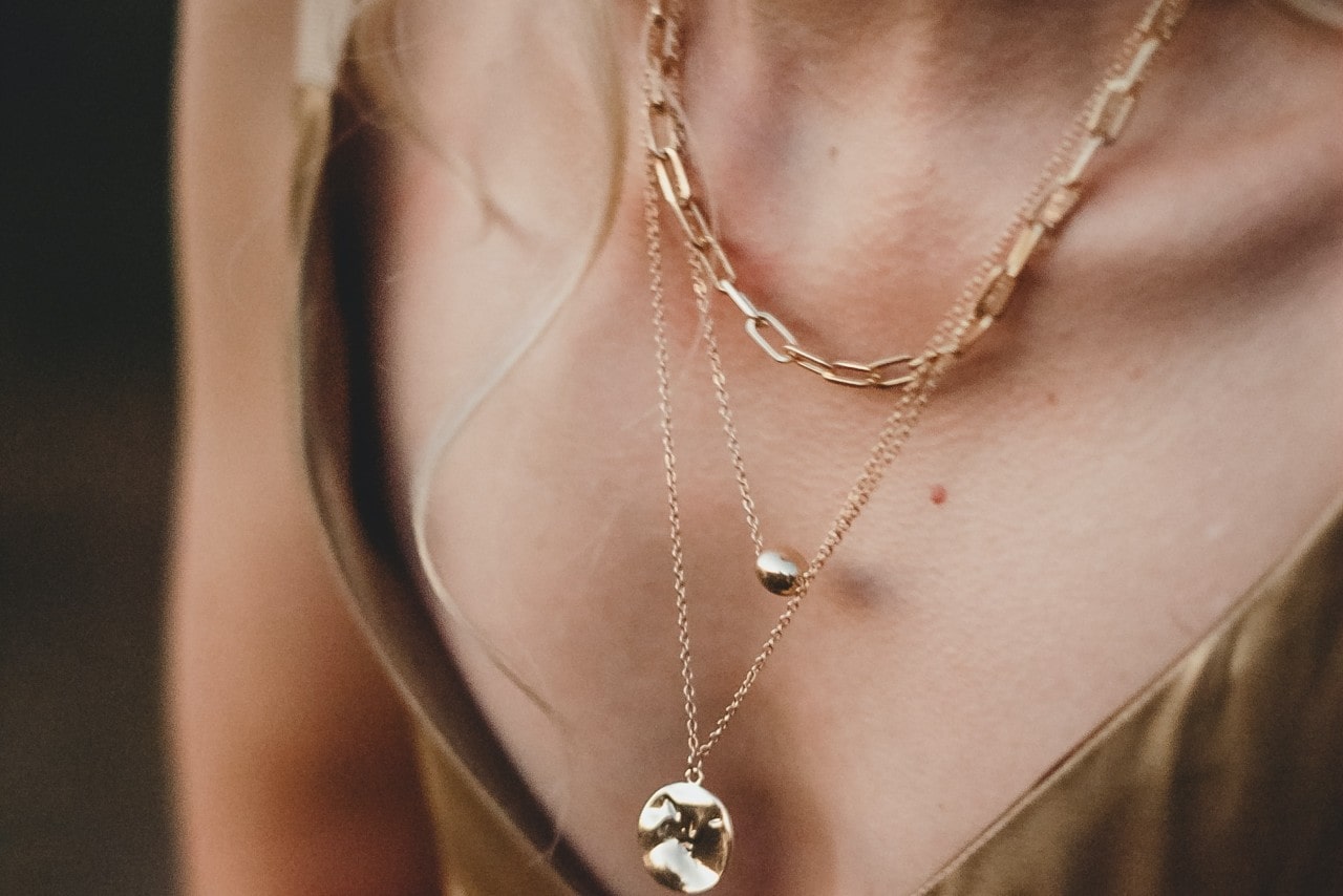 Close up image of a woman’s neckline, wearing three gold necklaces of varying lengths and styles