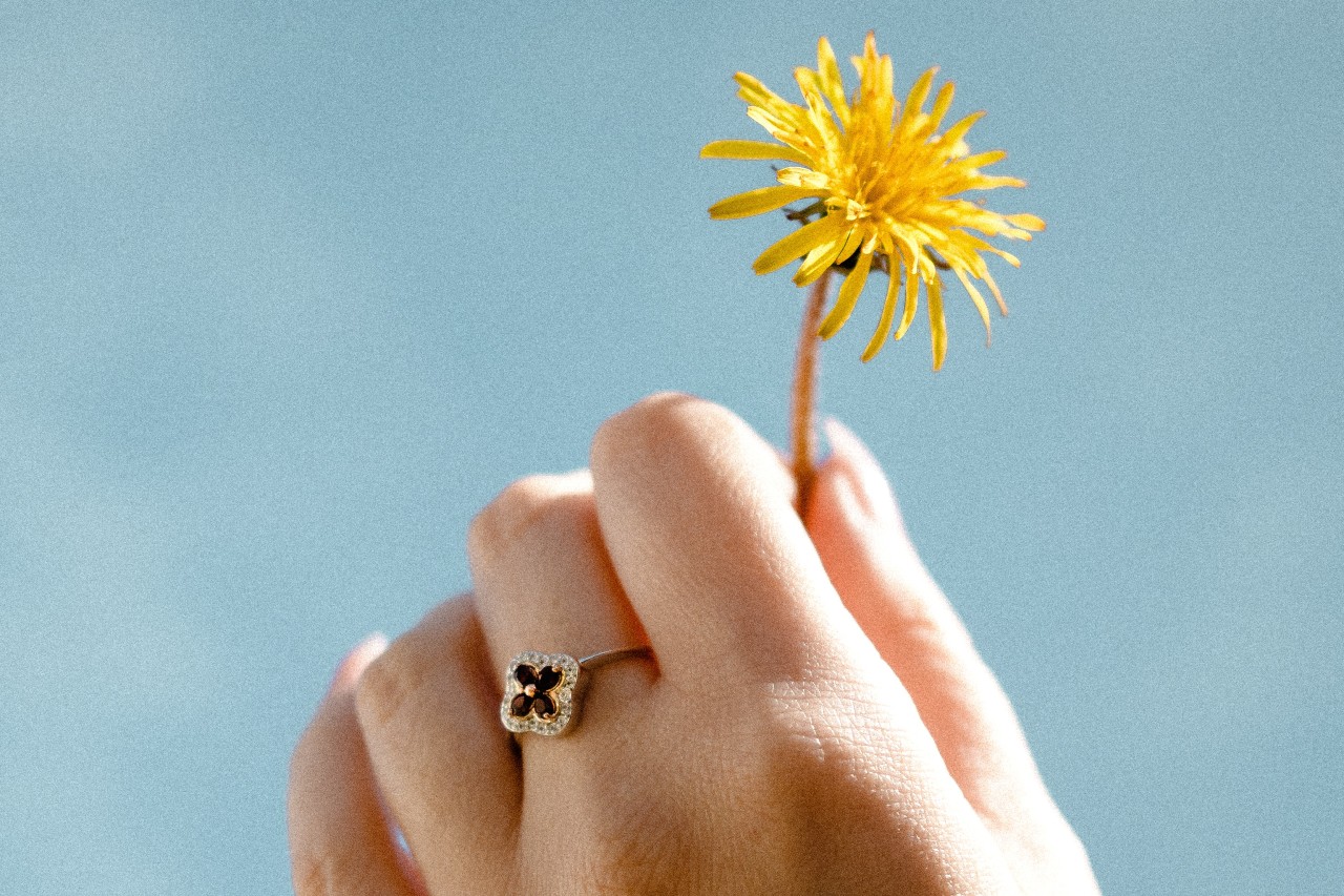 Woman wearing a floral fashion ring with diamond accents holding up a yellow flower