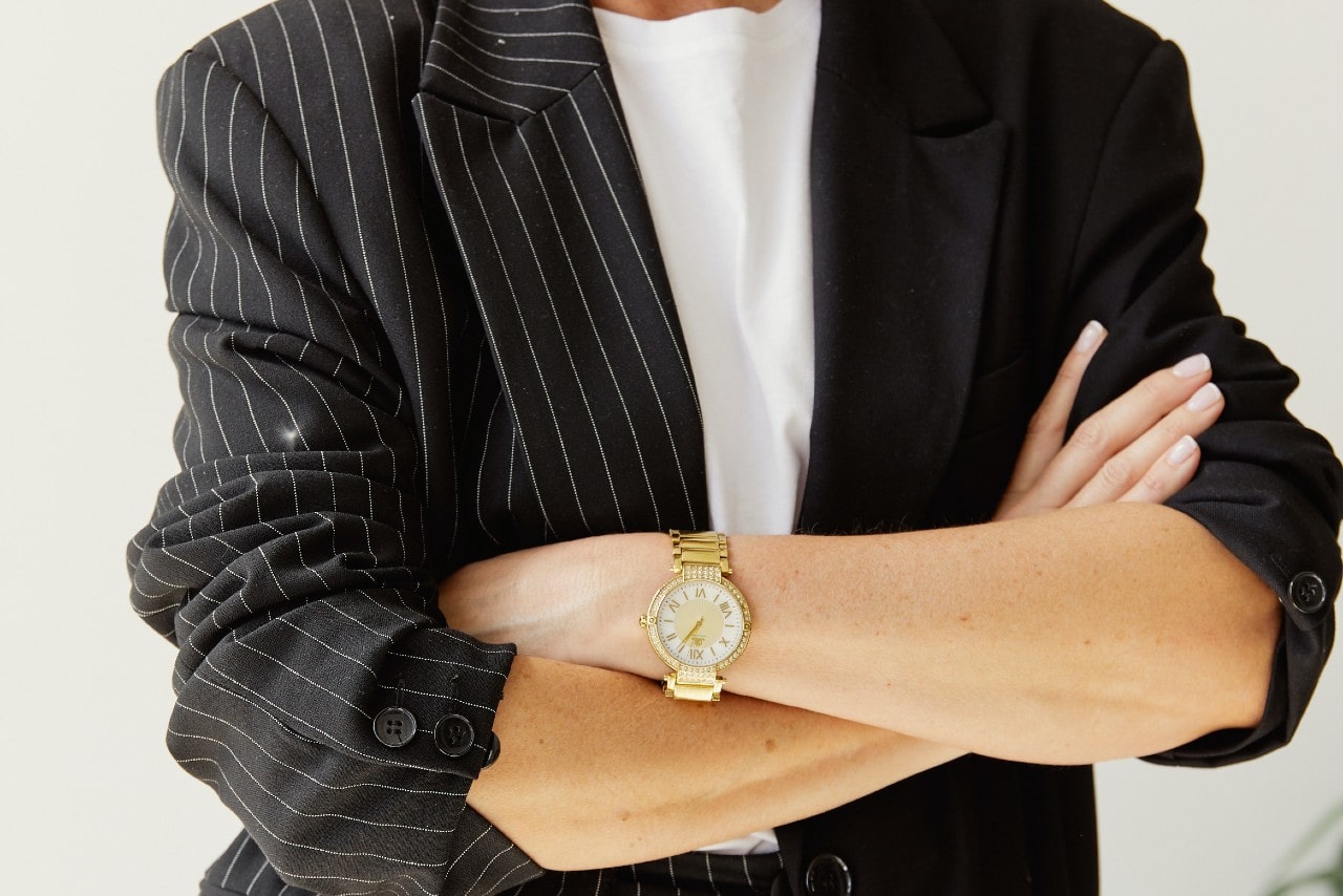 Person with their arms crossed, wearing a suit jacket and a gold watch