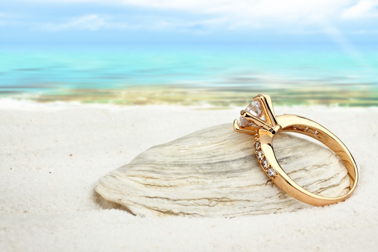Yellow gold and diamond engagement ring sitting on the beach