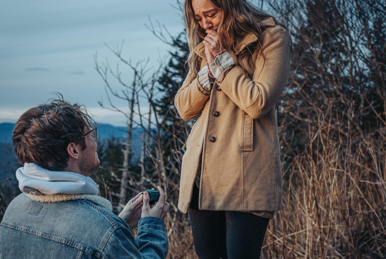 A man on one knee proposing to a lady outdoors