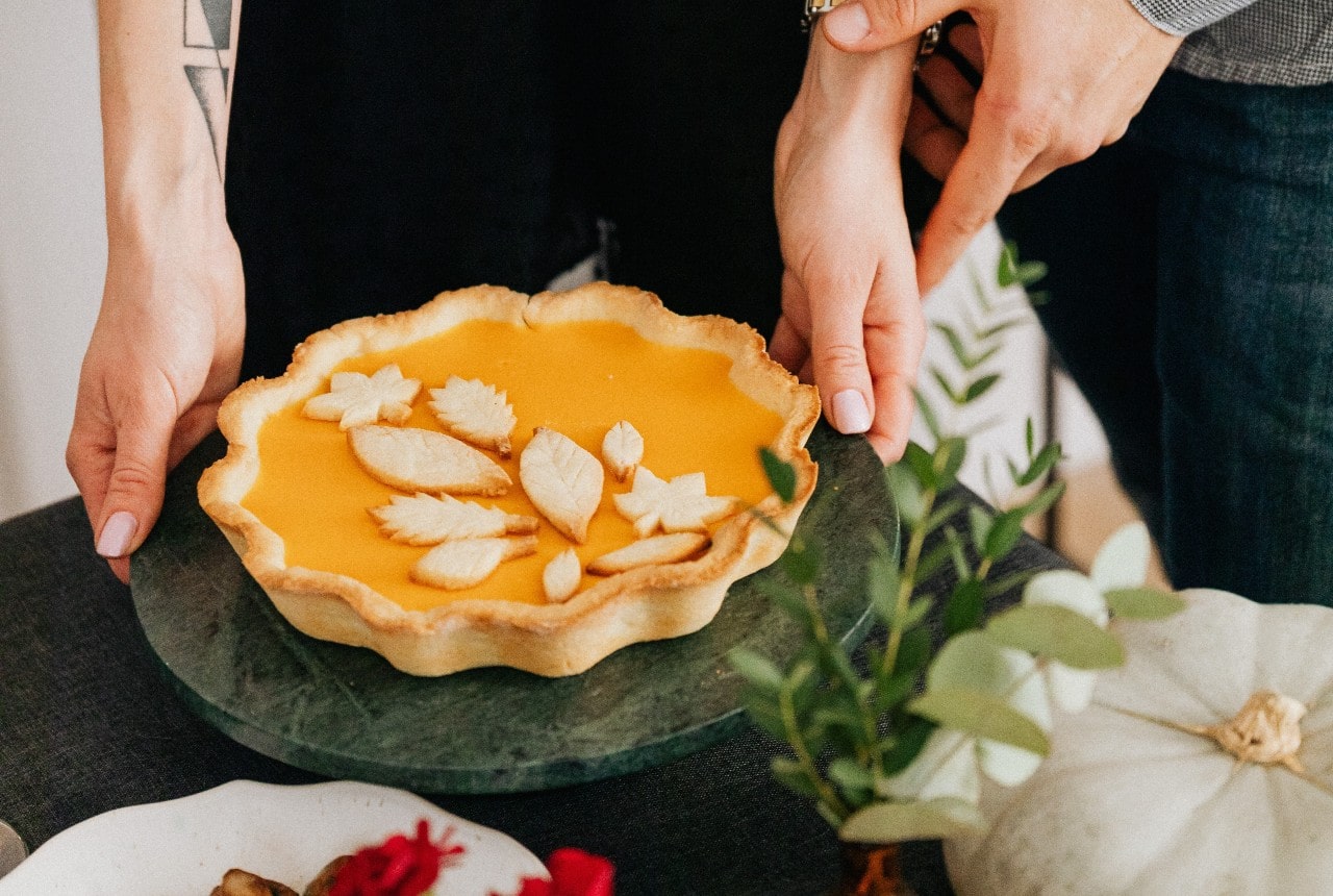 A man and a woman place a pumpkin pie on a festive table.
