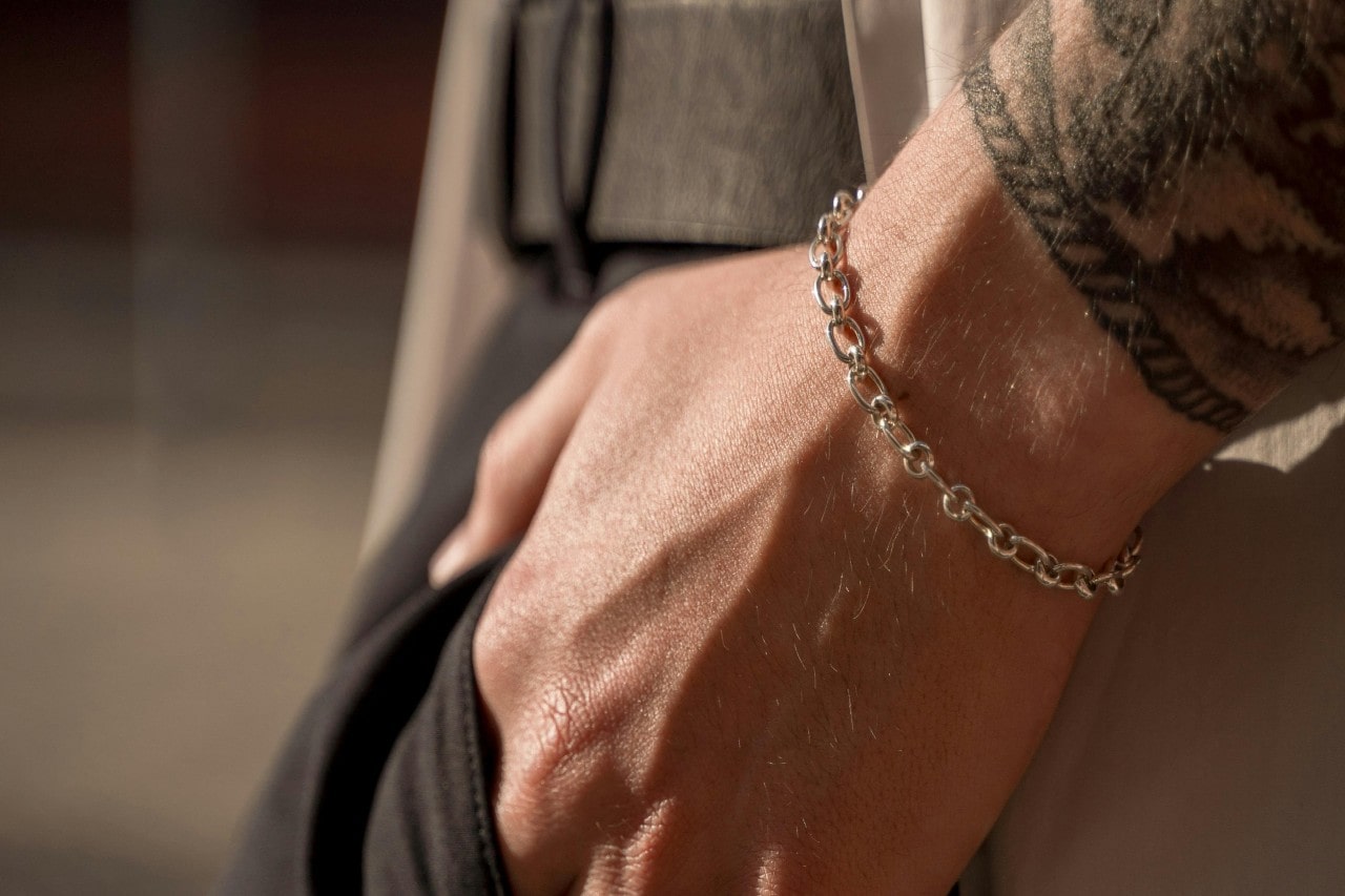 a man’s hand in his pocket, wearing a simple silver chain bracelet.