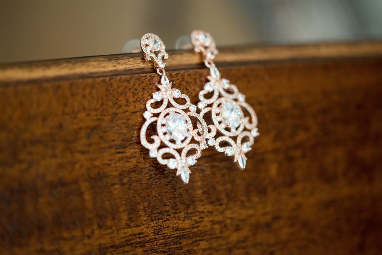 A close-up of an ornate pair of yellow gold and diamond earrings displayed over the side of a wooden surface.