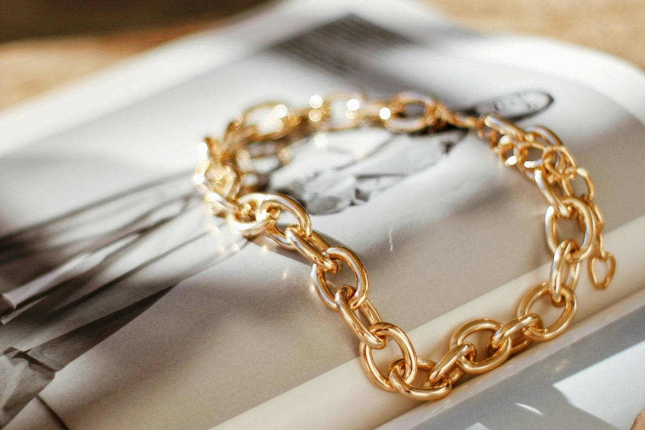 A close-up of an elegant gold chain bracelet displayed on top of a fashion magazine.