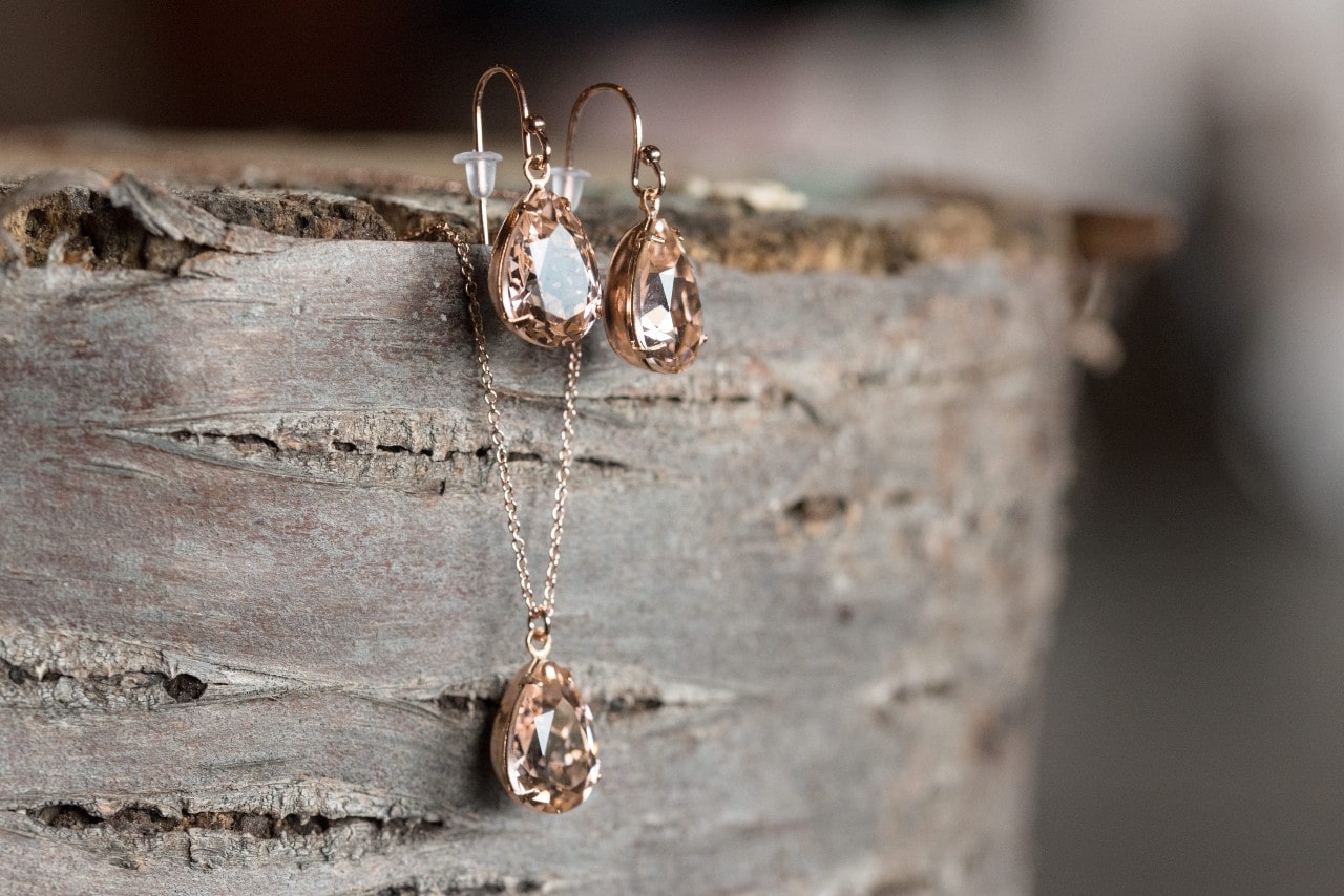 A close-up of a delicate pendant necklace and matching earrings, displayed on a cut tree.