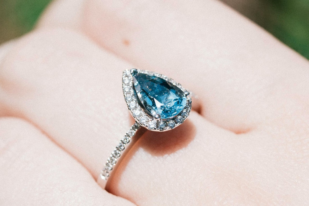 A close-up image of someone’s hand adorned with a white gold ring featuring a blue gemstone.