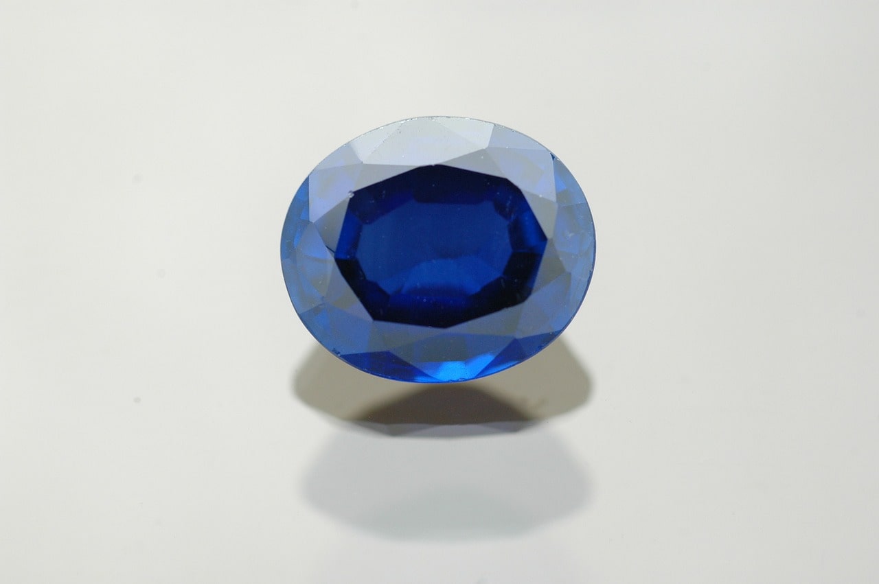 An oval cut, deep blue sapphire on a white surface.