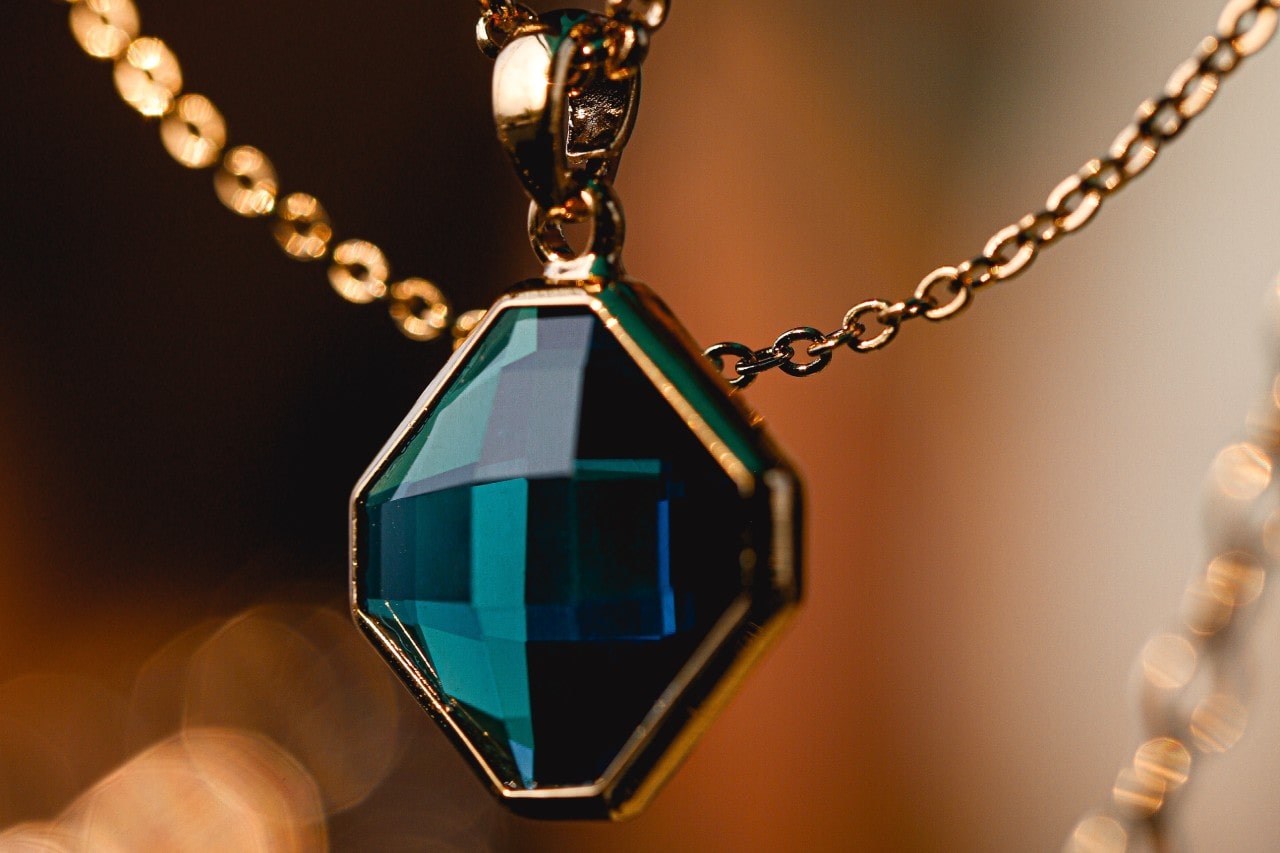 An elegant yellow gold pendant necklace featuring a deep blue-green gemstone.
