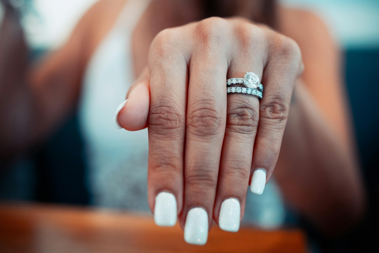 a woman’s extended hand, adorned with a diamond engagement ring and wedding band