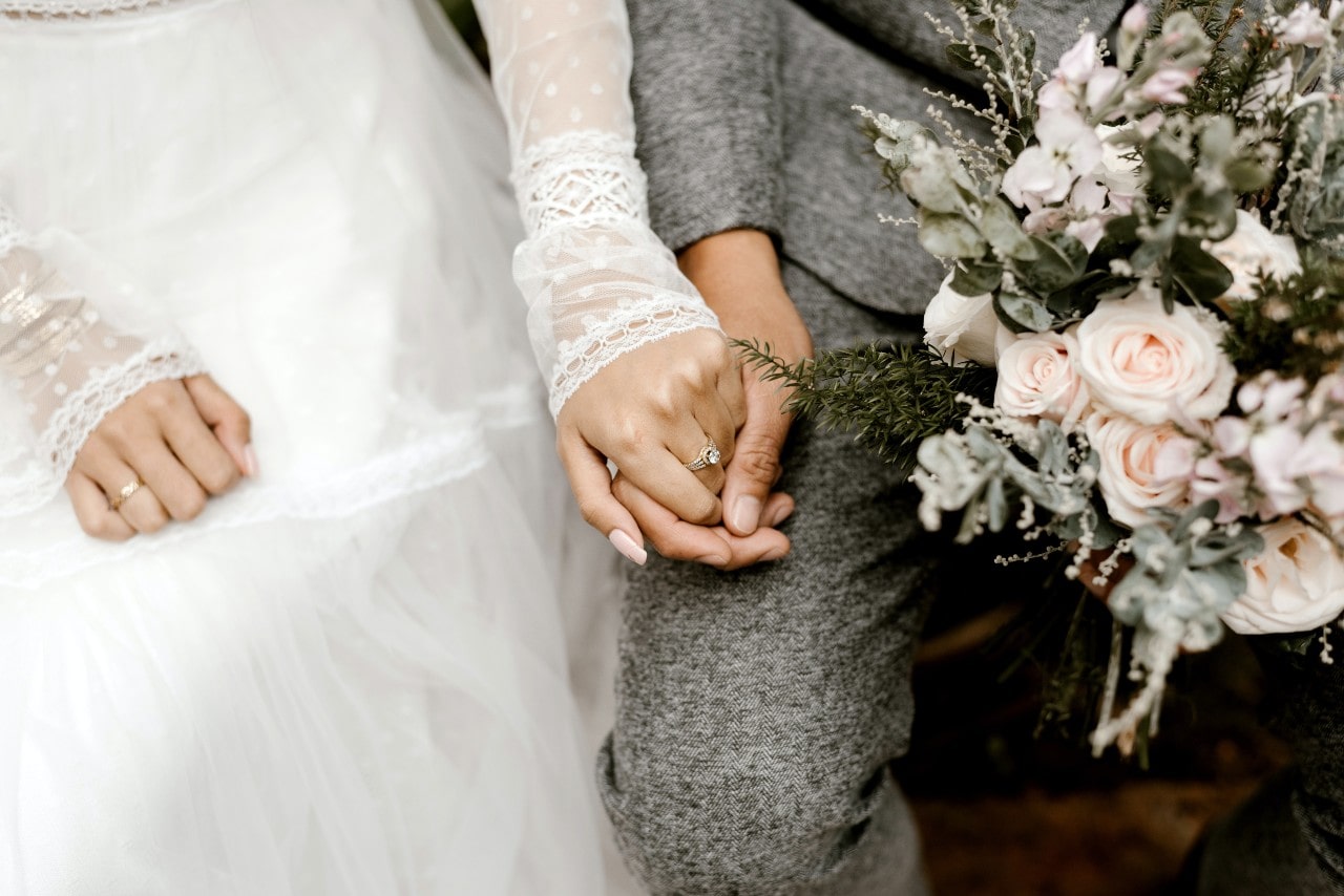 Bride in white and groom in grey sharing a quiet moment as her diamond ring catches the light with a bouquet in his hand. Bride in white and groom in grey sharing a quiet moment as her diamond ring catches the light with a bouquet in his hand.