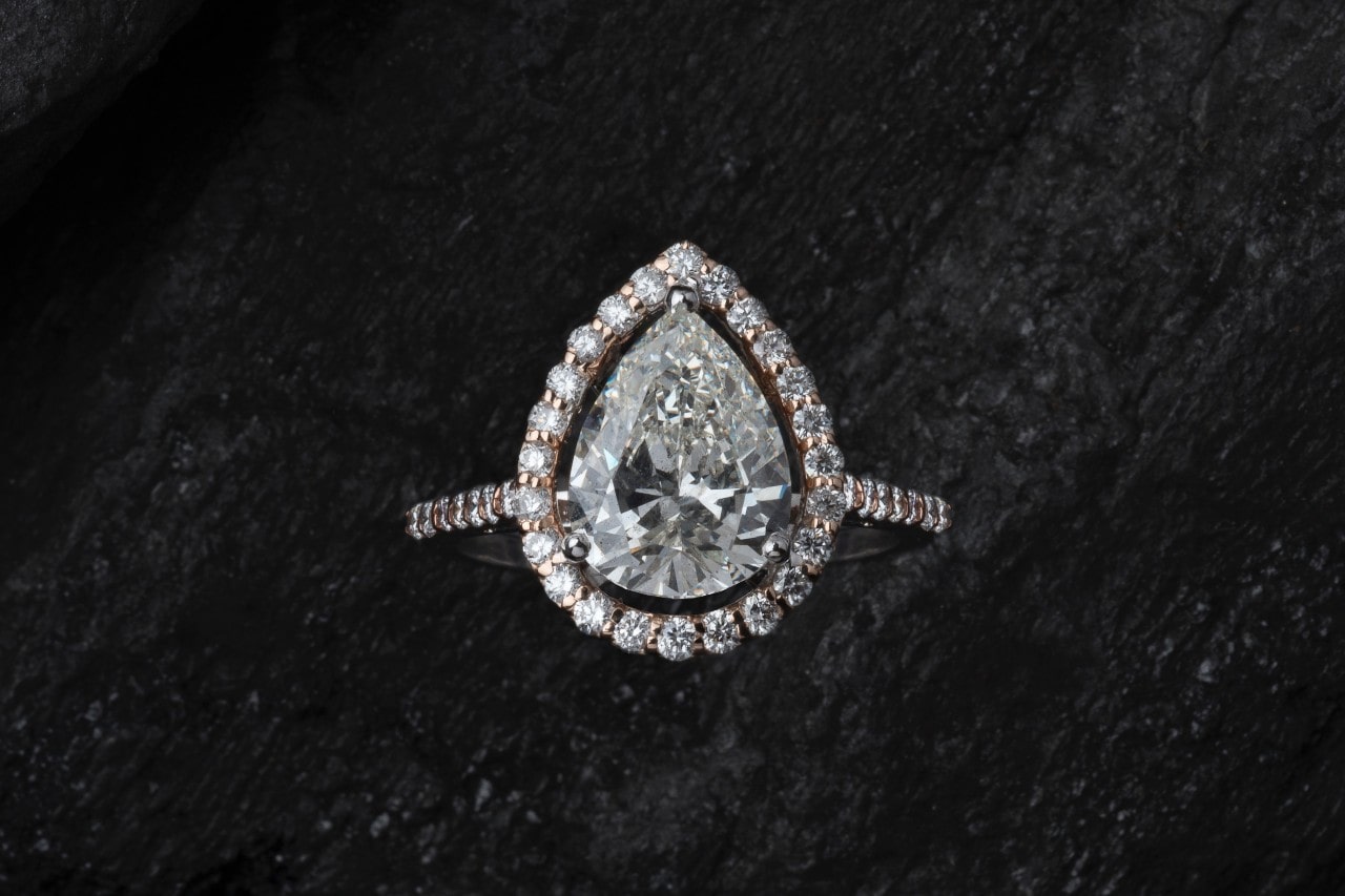 A close up of pear-shaped diamond ring with center stone and side accent diamonds resting on black background A close up of pear-shaped diamond ring with center stone and side accent diamonds resting on black background