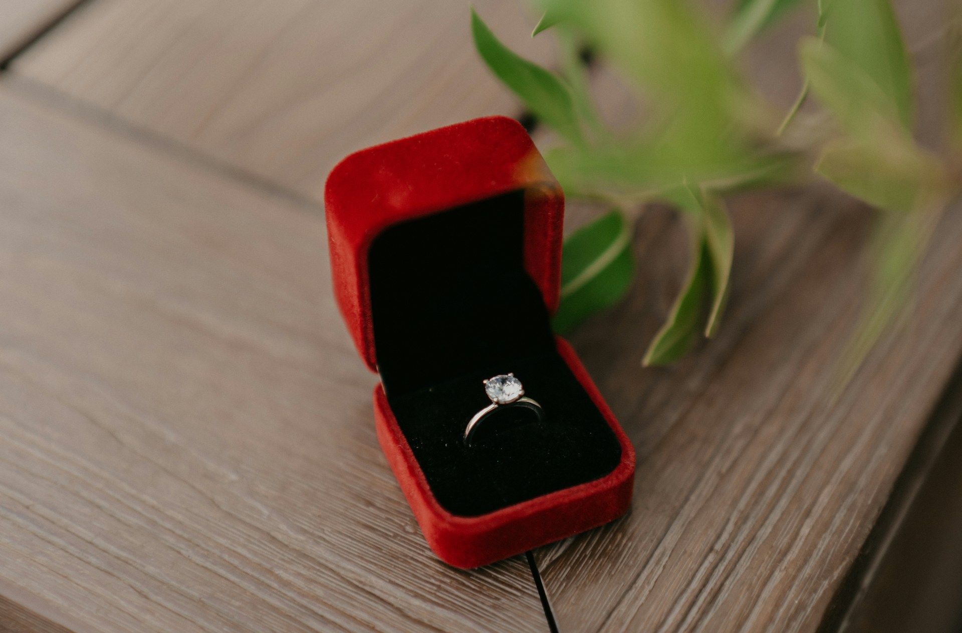 A close-up of an elegant solitaire engagement ring presented in a red velvet ring box.