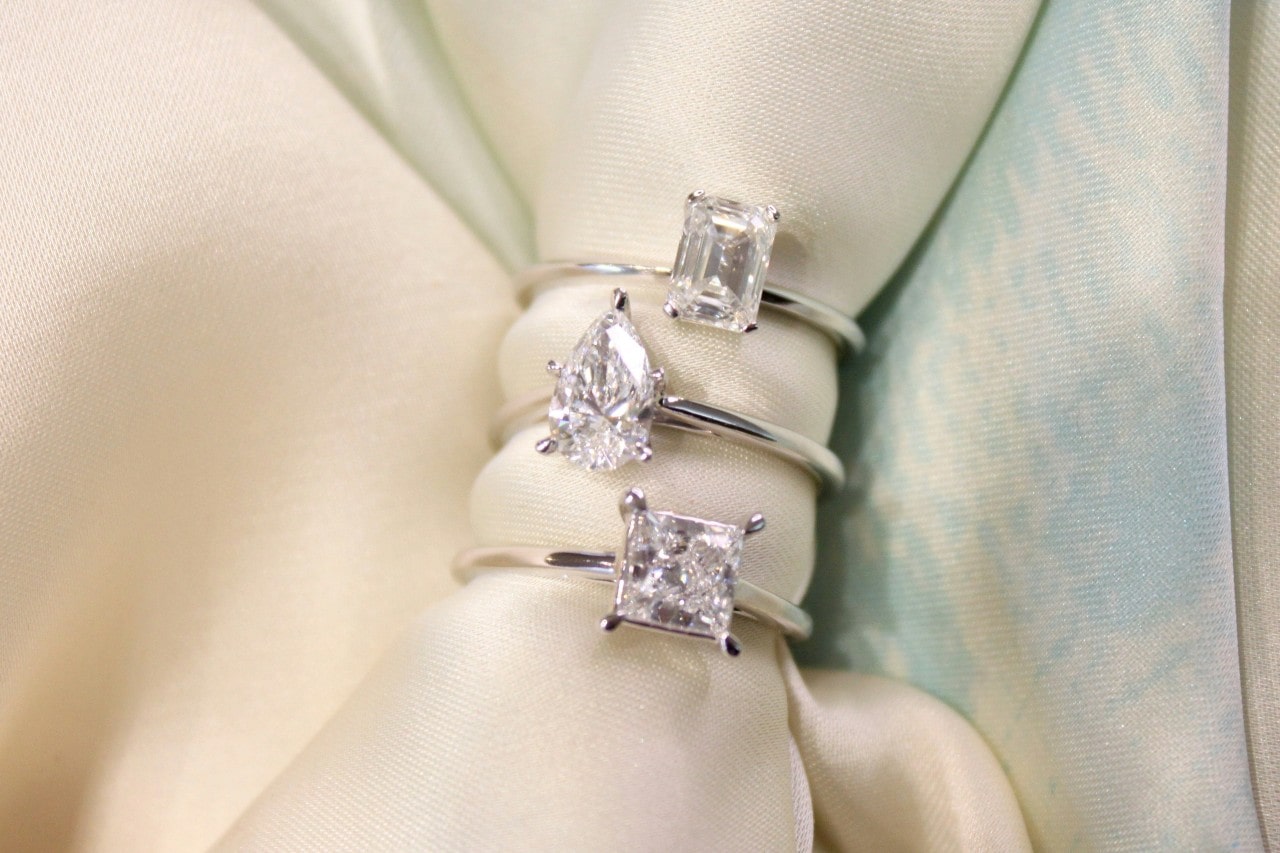 A close-up of three solitaire diamond rings displayed on a cloth napkin.