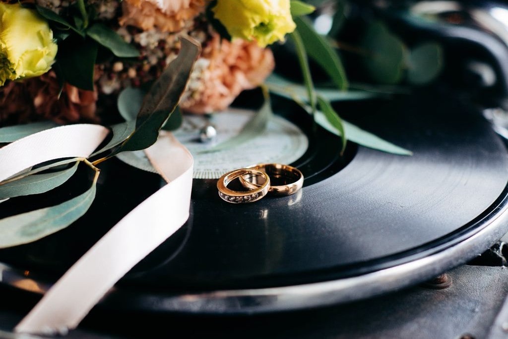 Two stunning wedding bands displayed on a vinyl record before a lovely bouquet.