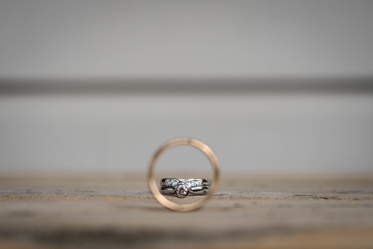 Two distinct wedding bands displayed on a rocky surface, the woman’s ring visible through the man’s.