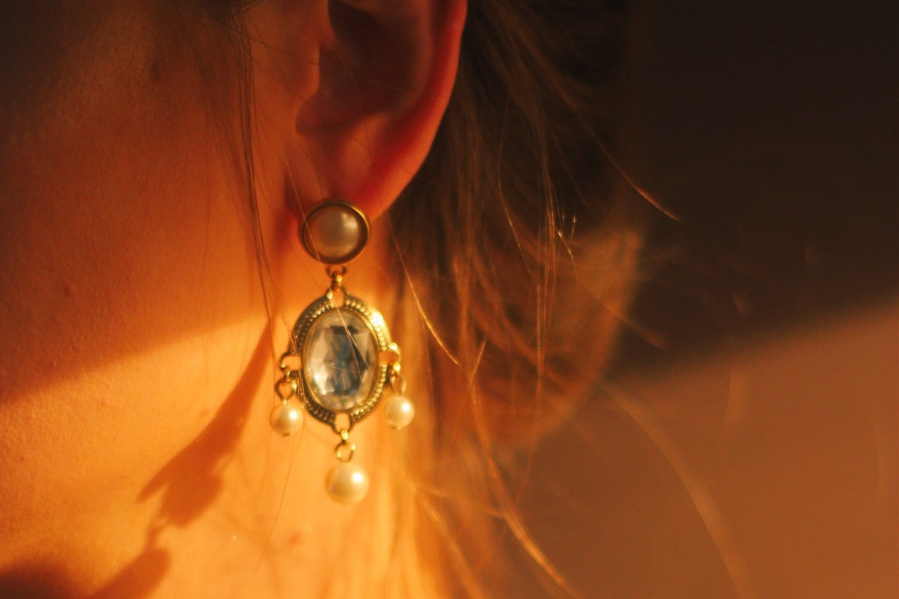 A close-up of a woman’s ear adorned an elegant earring with an oval diamond center stone.