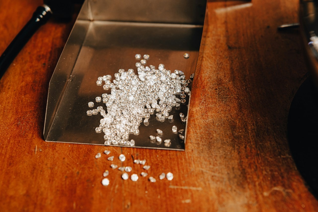 A large assortment of diamonds in a metal tray, atop a wooden surface.