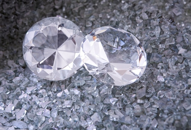 A close-up of two colorless round cut diamonds displayed atop diamond trimmings.