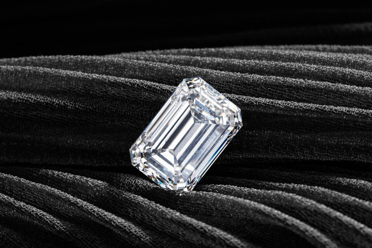 A close-up of a stunning emerald cut diamond on a dark fabric backdrop.