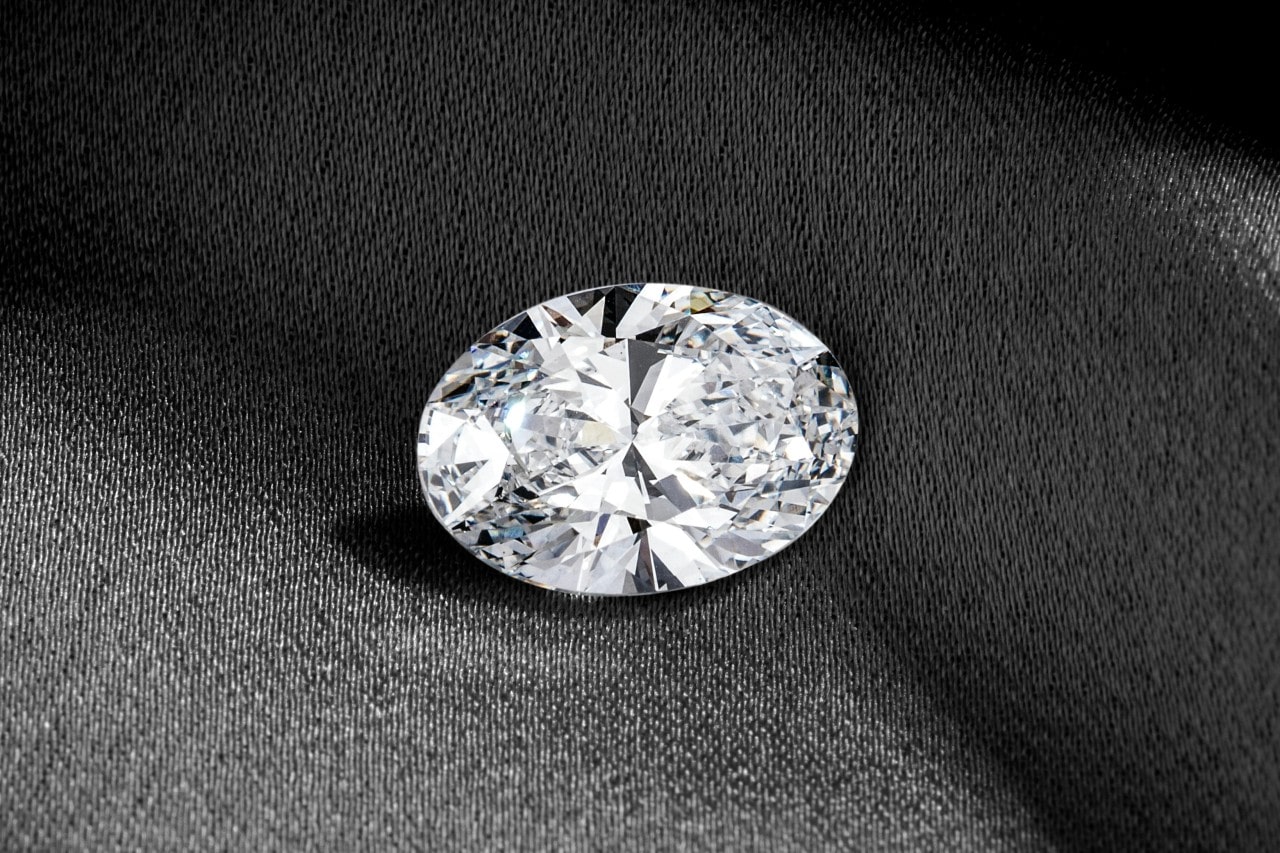 An elegant oval cut diamond on a dark fabric background.